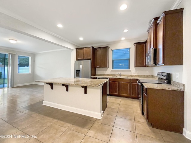 kitchen with a breakfast bar, crown molding, light tile patterned floors, appliances with stainless steel finishes, and a kitchen island