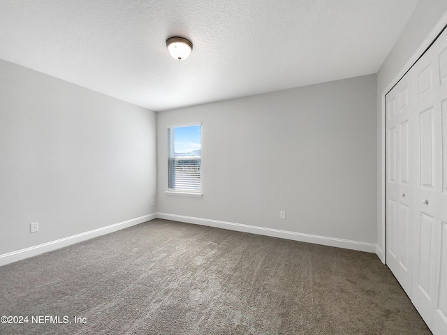 unfurnished bedroom featuring dark colored carpet, a textured ceiling, and a closet