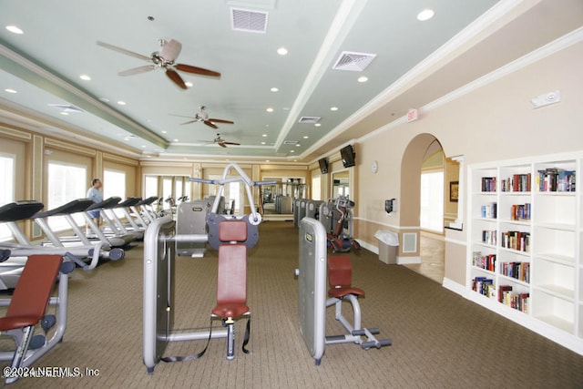 exercise room featuring ceiling fan, carpet floors, ornamental molding, and a tray ceiling