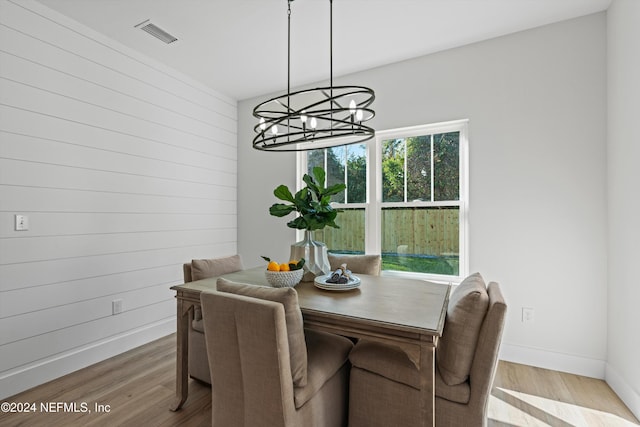 dining room with wood walls, wood-type flooring, and an inviting chandelier