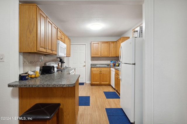 kitchen with white appliances, light wood-type flooring, tasteful backsplash, kitchen peninsula, and a breakfast bar area