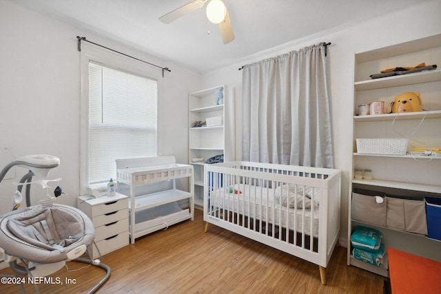 bedroom featuring ceiling fan, hardwood / wood-style floors, and a crib