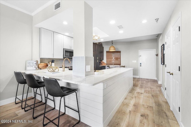 kitchen featuring kitchen peninsula, appliances with stainless steel finishes, a kitchen bar, and light wood-type flooring