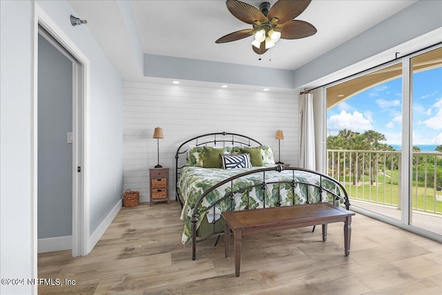 bedroom featuring access to outside, ceiling fan, light hardwood / wood-style floors, and wood walls