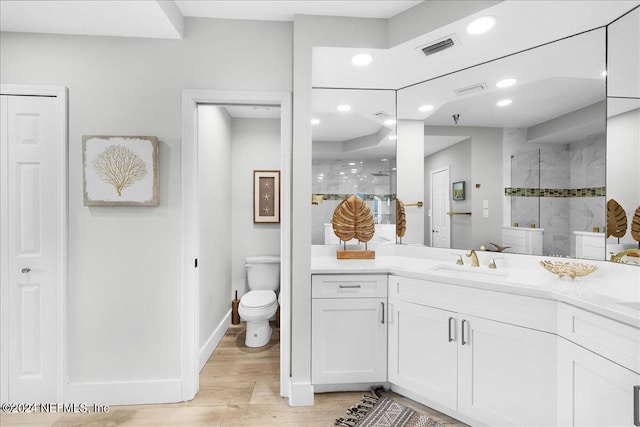 bathroom featuring hardwood / wood-style flooring, toilet, a tile shower, and vanity