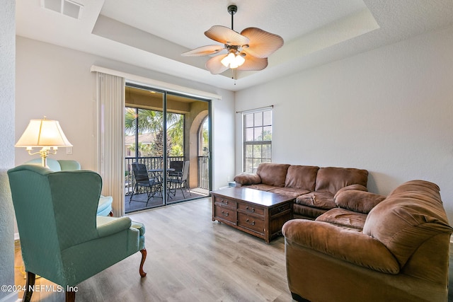 living room featuring ceiling fan, light hardwood / wood-style flooring, and a tray ceiling