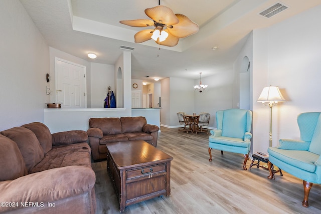 living room featuring ceiling fan with notable chandelier, light wood-type flooring, and a tray ceiling