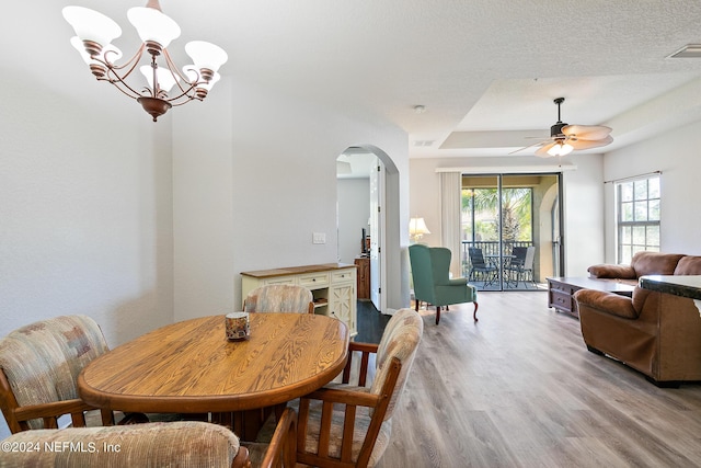 dining area with ceiling fan with notable chandelier, a textured ceiling, and light wood-type flooring