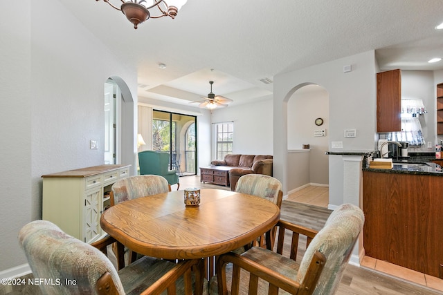 dining space with a textured ceiling, a raised ceiling, ceiling fan, sink, and light hardwood / wood-style floors