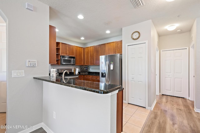 kitchen with kitchen peninsula, appliances with stainless steel finishes, light wood-type flooring, and dark stone countertops