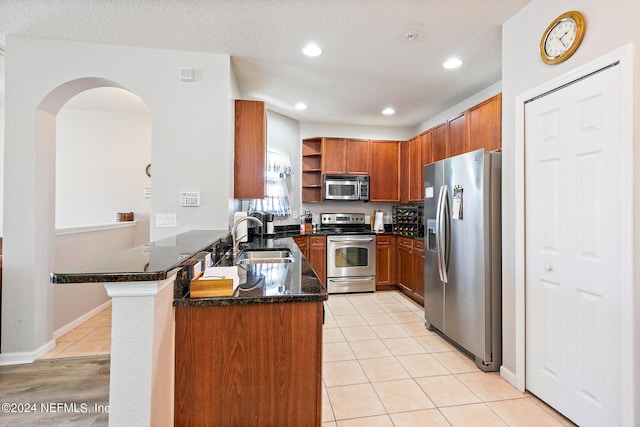 kitchen with sink, kitchen peninsula, dark stone countertops, a textured ceiling, and appliances with stainless steel finishes