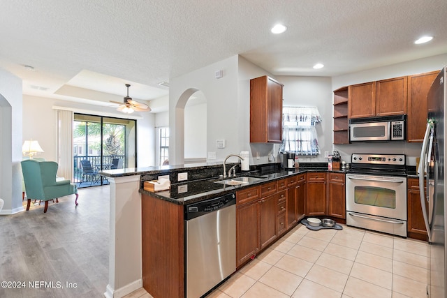 kitchen with kitchen peninsula, appliances with stainless steel finishes, a textured ceiling, sink, and dark stone countertops