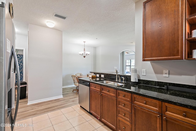 kitchen with sink, light hardwood / wood-style flooring, dark stone counters, decorative light fixtures, and appliances with stainless steel finishes