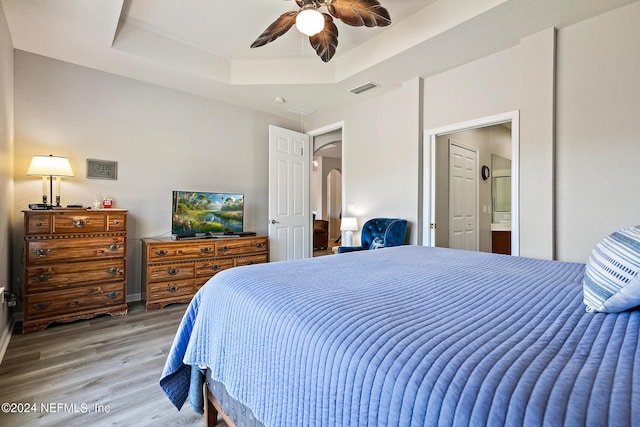 bedroom with hardwood / wood-style floors, ceiling fan, connected bathroom, and a tray ceiling