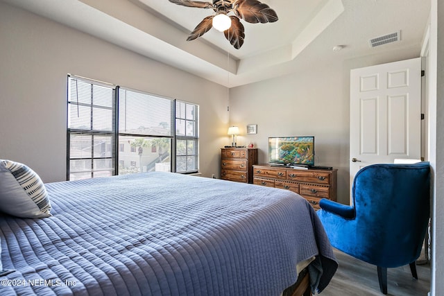 bedroom with ceiling fan, wood-type flooring, and a tray ceiling