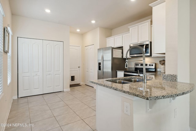 kitchen featuring kitchen peninsula, stainless steel appliances, light tile patterned floors, stone counters, and white cabinetry