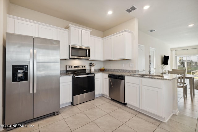 kitchen with light tile patterned floors, white cabinetry, light stone counters, kitchen peninsula, and stainless steel appliances