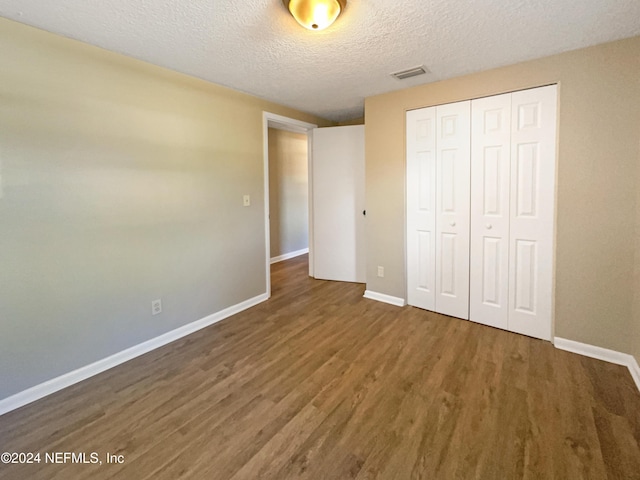 unfurnished bedroom with a textured ceiling, dark hardwood / wood-style floors, and a closet