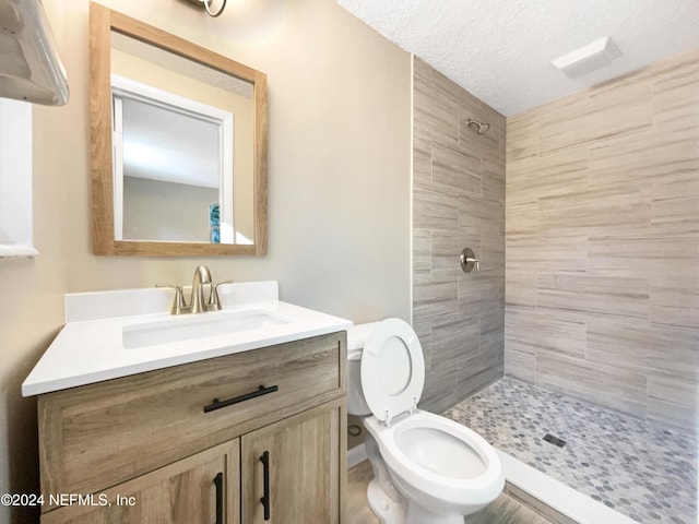 bathroom with vanity, a textured ceiling, tiled shower, and toilet