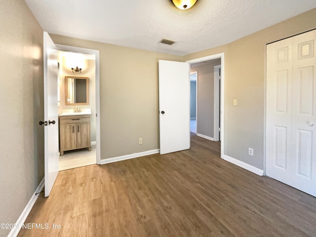 unfurnished bedroom with connected bathroom, sink, hardwood / wood-style floors, a textured ceiling, and a closet