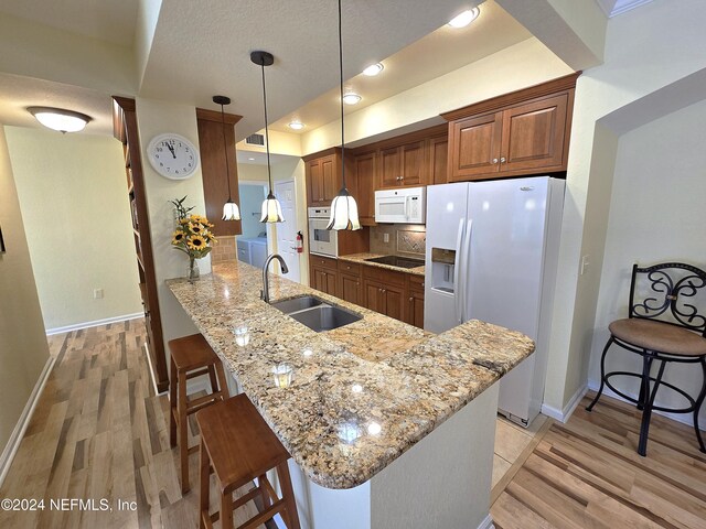 kitchen with white appliances, a kitchen breakfast bar, sink, light hardwood / wood-style floors, and kitchen peninsula