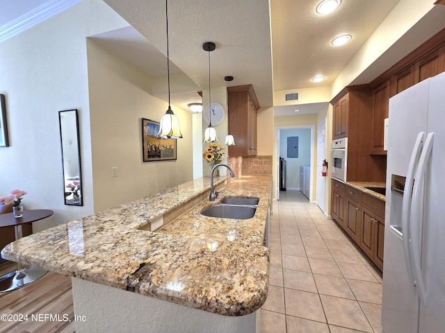 kitchen featuring kitchen peninsula, light stone countertops, white appliances, sink, and hanging light fixtures