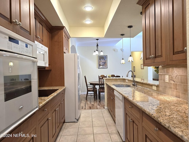 kitchen with decorative backsplash, light stone countertops, white appliances, sink, and a chandelier