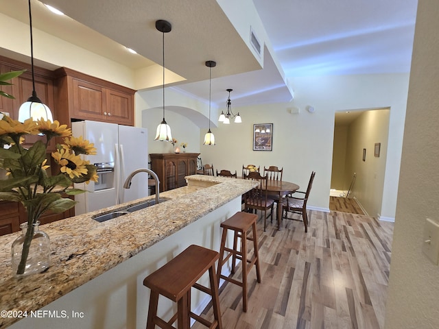 kitchen featuring a kitchen breakfast bar, light wood-type flooring, light stone counters, sink, and white fridge with ice dispenser