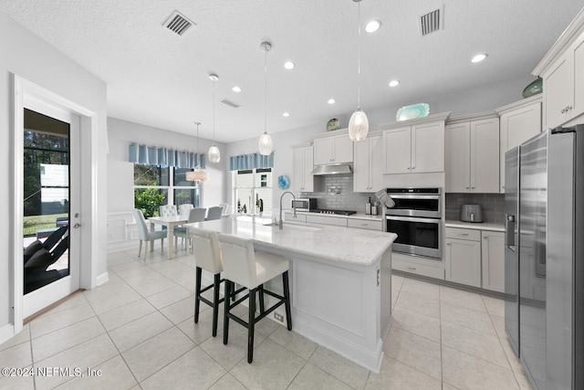 kitchen with backsplash, a center island with sink, sink, hanging light fixtures, and appliances with stainless steel finishes