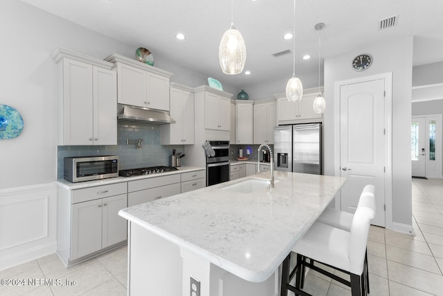 kitchen with sink, an island with sink, pendant lighting, a breakfast bar area, and appliances with stainless steel finishes