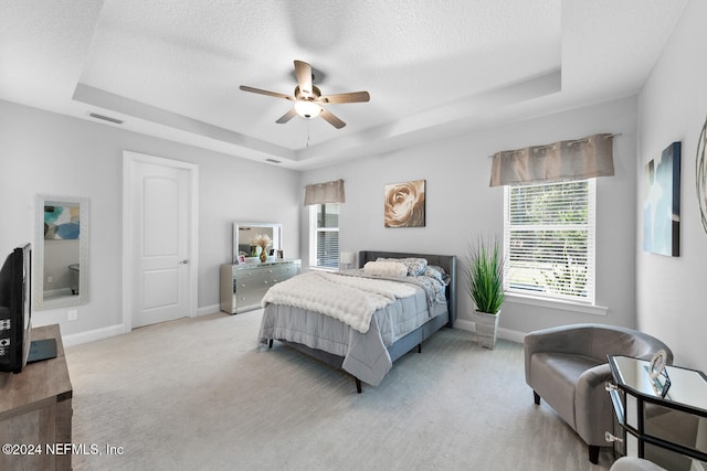 carpeted bedroom with a textured ceiling, a tray ceiling, and ceiling fan