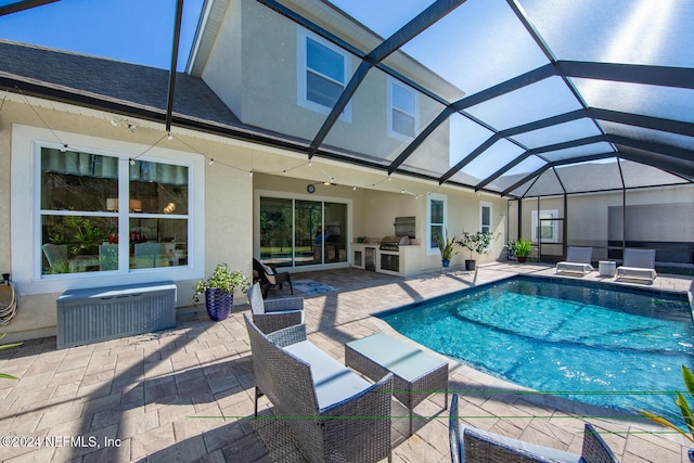 view of pool with an outdoor kitchen, area for grilling, a patio area, and glass enclosure