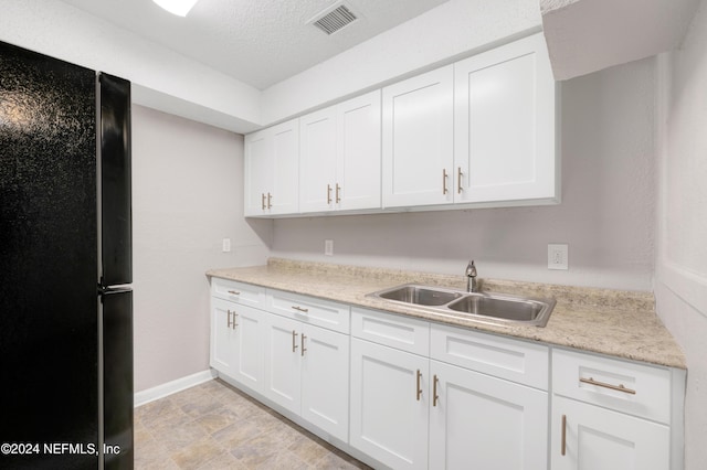 kitchen with white cabinets, a textured ceiling, black fridge, and sink