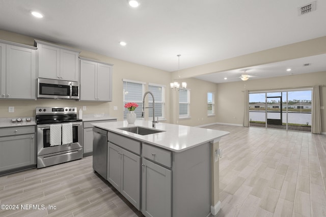 kitchen featuring ceiling fan with notable chandelier, stainless steel appliances, sink, a kitchen island with sink, and gray cabinetry