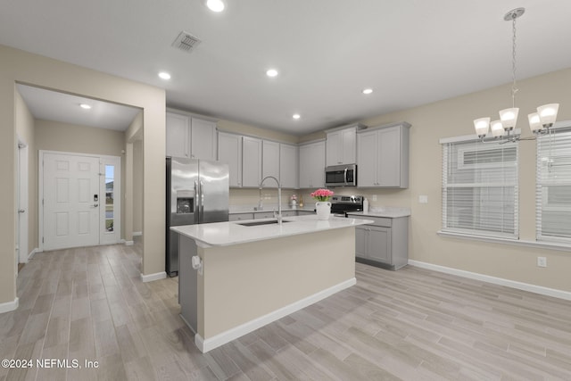 kitchen featuring gray cabinetry, sink, an inviting chandelier, stainless steel appliances, and a center island with sink