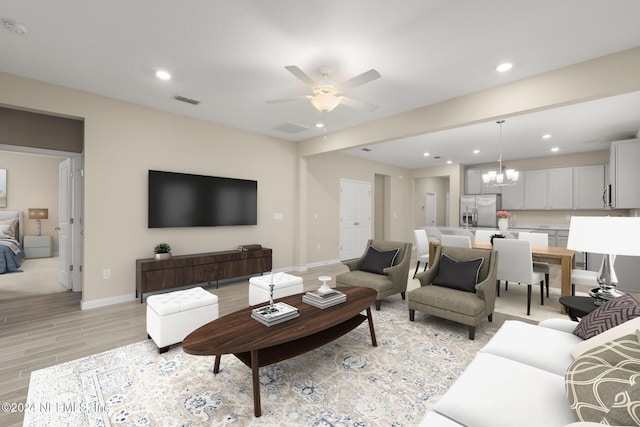 living room with light wood-type flooring and ceiling fan with notable chandelier