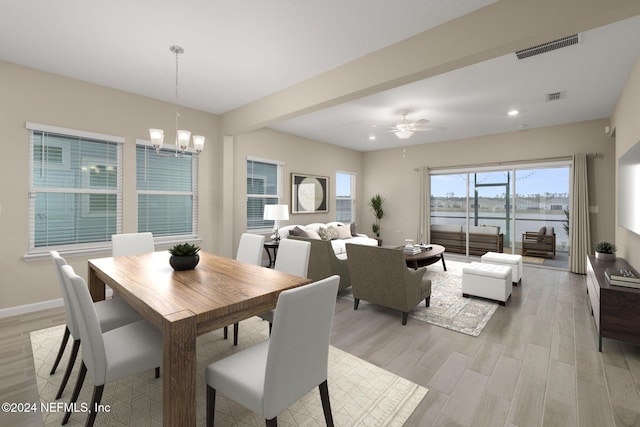 dining room with ceiling fan with notable chandelier, a water view, and light hardwood / wood-style floors