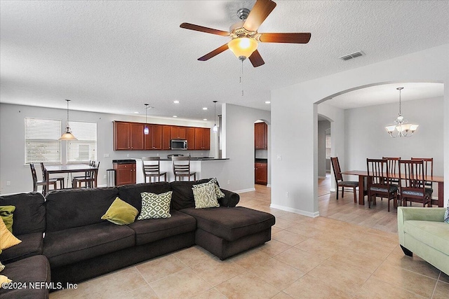 tiled living room with a textured ceiling and ceiling fan with notable chandelier