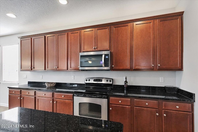 kitchen with a textured ceiling, dark stone countertops, and stainless steel appliances