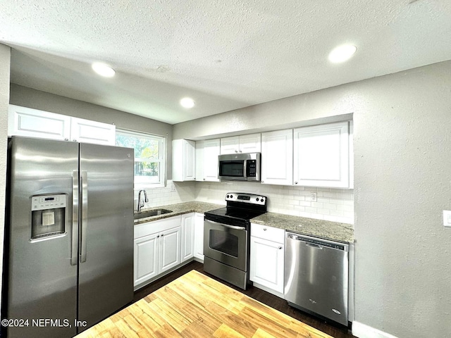 kitchen featuring appliances with stainless steel finishes, backsplash, sink, hardwood / wood-style flooring, and white cabinetry