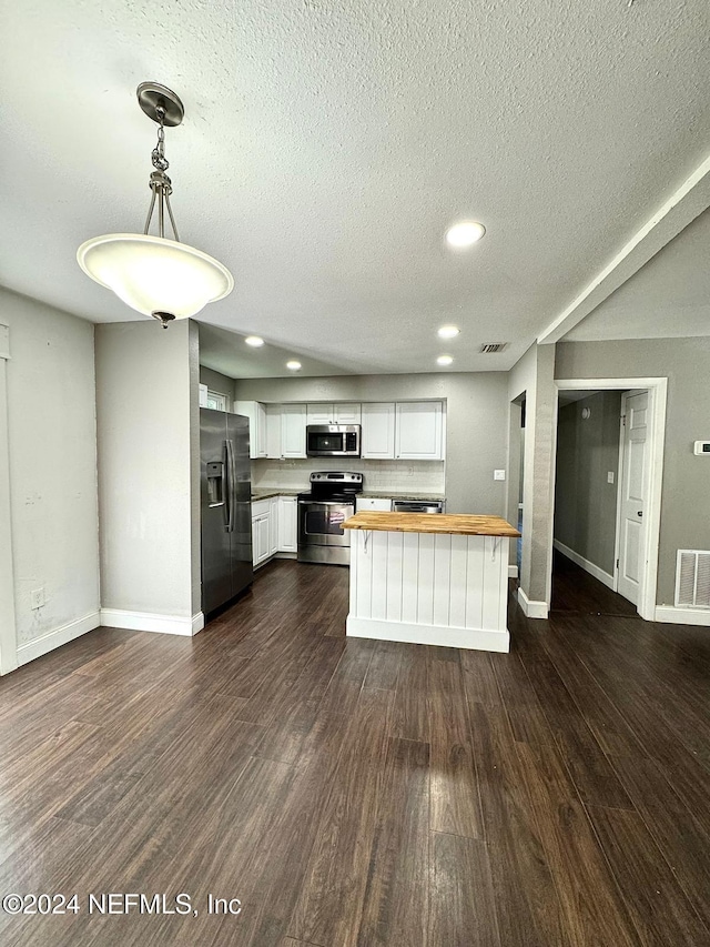 kitchen featuring dark wood-type flooring, white cabinets, hanging light fixtures, appliances with stainless steel finishes, and butcher block counters