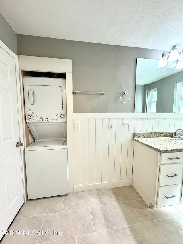 laundry area featuring a textured ceiling, sink, light tile patterned floors, and stacked washer and dryer