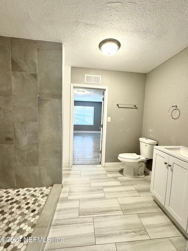 bathroom with vanity, toilet, a textured ceiling, and walk in shower