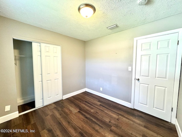 unfurnished bedroom with a textured ceiling, dark hardwood / wood-style flooring, and a closet