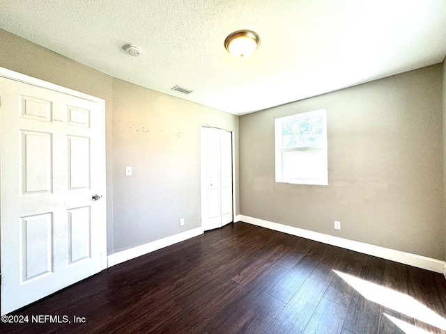 unfurnished bedroom featuring a textured ceiling, a closet, and dark hardwood / wood-style floors