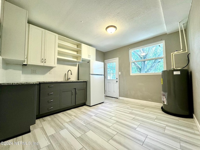 kitchen with decorative backsplash, light stone countertops, water heater, white fridge, and white cabinetry