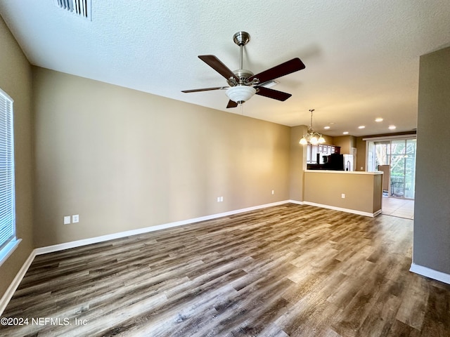 unfurnished living room featuring ceiling fan with notable chandelier, wood-type flooring, and a textured ceiling