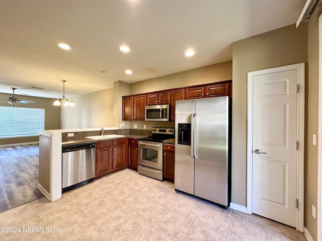 kitchen featuring kitchen peninsula, ceiling fan with notable chandelier, stainless steel appliances, sink, and hanging light fixtures