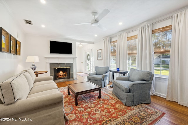 living room with hardwood / wood-style flooring, ceiling fan, ornamental molding, and a tiled fireplace