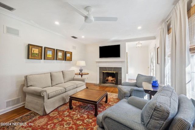 living room with hardwood / wood-style flooring, ceiling fan, crown molding, and a tile fireplace